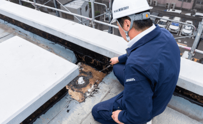 屋上の防水層を調査する建築士が破損箇所を確認している様子
