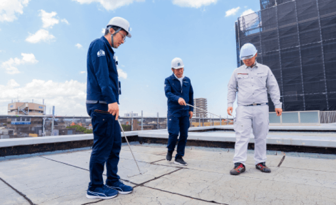 屋上を調査する建築士たち。打診棒を使って防水層の状態を確認している様子