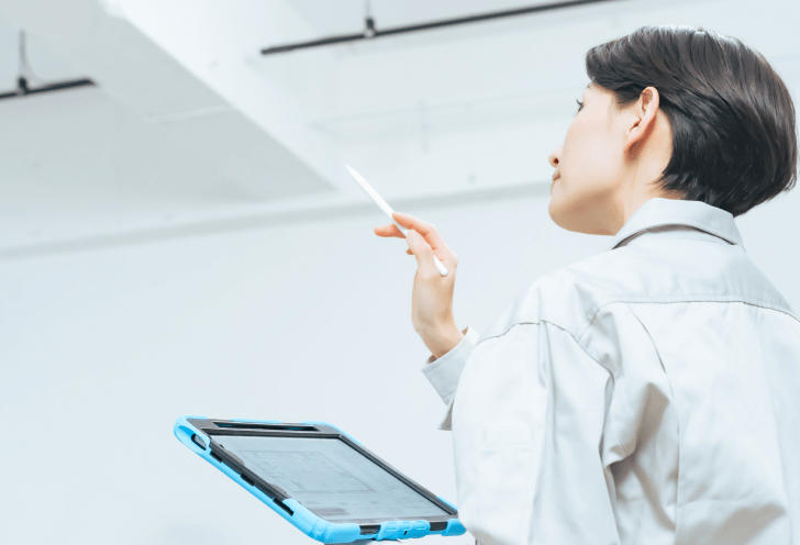 建物内部の天井部分をタブレット片手に点検している建築士の後ろ姿